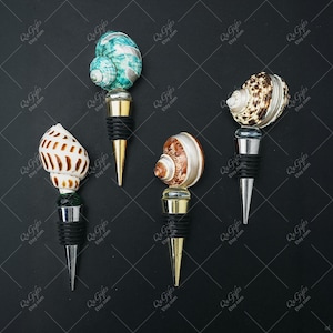 May include: Four decorative wine bottle stoppers with seashell designs. Each stopper features a different shell, including a blue and white spiral, and a brown and white spotted shell. The stoppers have gold or silver metal bases.