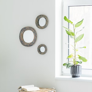 May include: Three circular wall mirrors with textured, dark blue and brown concentric ring frames. The mirrors are arranged in a cluster on a plain wall, featuring reflective glass centers and distinct, layered, ridged outer borders.