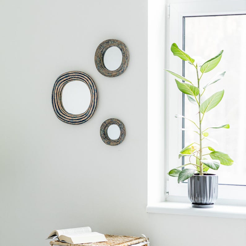 May include: Three circular wall mirrors with textured, dark blue and brown concentric ring frames. The mirrors are arranged in a cluster on a plain wall, featuring reflective glass centers and distinct, layered, ridged outer borders.