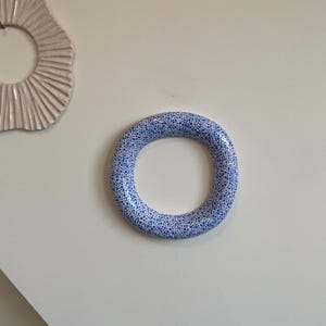 Puede incluir: Un anillo de cer&aacute;mica blanca con un patr&oacute;n moteado azul. El anillo es grueso y tiene un acabado liso y brillante.