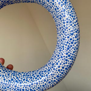 Puede incluir: Un anillo de cer&aacute;mica blanca con un patr&oacute;n de lunares azules. El anillo es grueso y tiene un acabado brillante.