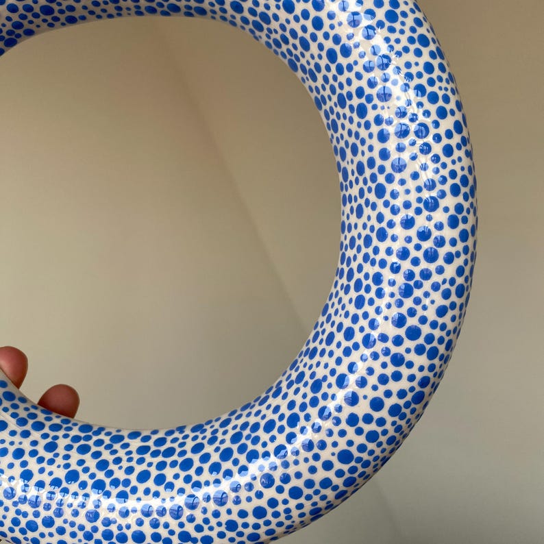 Puede incluir: Un anillo de cer&aacute;mica blanca con un patr&oacute;n de lunares azules. El anillo es grueso y tiene un acabado brillante.