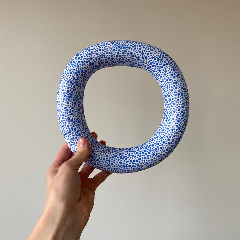 Puede incluir: Un anillo de cer&aacute;mica blanca con un patr&oacute;n de lunares azules. El anillo es grueso y tiene una gran abertura.