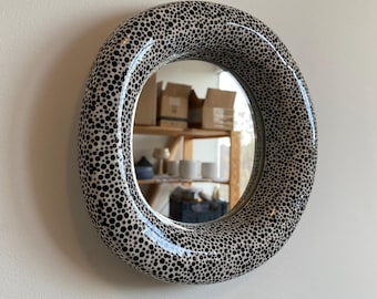 May include: A round wall mirror featuring a thick, rounded frame with a glossy white finish covered in a dense pattern of black polka dots of varying sizes. The reflective glass surface is centered within the circular frame, creating a bold contrast.