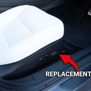 Könnte beinhalten: Nahaufnahme eines schwarzen Autoinnenraums mit einem weißen Ledersitz. An der Seite des Sitzes ist ein schwarzer Plastikknopf sichtbar, der mit "REPLACEMENT" beschriftet ist.
