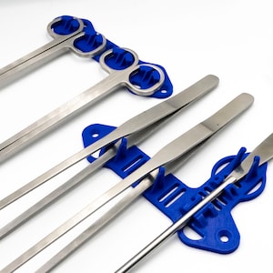 Pode incluir: Um conjunto de cinco ferramentas cir&uacute;rgicas com al&ccedil;as de pl&aacute;stico azul, incluindo pin&ccedil;as, f&oacute;rceps e uma esp&aacute;tula, s&atilde;o exibidas em um suporte de pl&aacute;stico azul.
