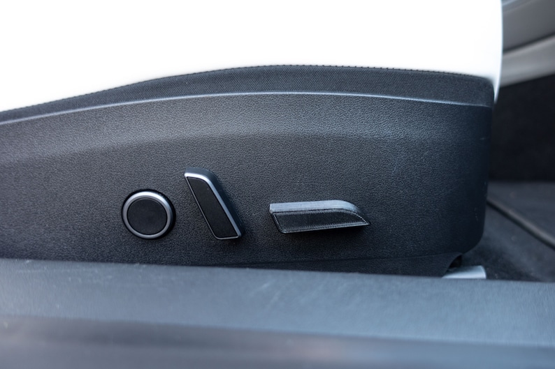 Op de afbeelding: Close-up van zwarte autostoelbediening. De bedieningselementen omvatten een ronde knop en twee rechthoekige knoppen.