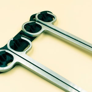 Pode incluir: Duas ferramentas de metal prateado com al&ccedil;as de pl&aacute;stico preto. As ferramentas est&atilde;o presas a um suporte de pl&aacute;stico preto.