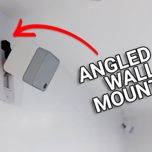 May include: An angled wall mount, white and gray, is installed on a white wall. The mount is connected to an electrical outlet. The text "ANGLED WALL MOUNT" is displayed in black and white.