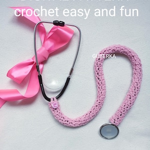 Peut inclure: Un cache-stéthoscope rose au crochet avec un nœud rose assorti et le texte "DIGITAL PATTERN crochet easy and fun". Le stéthoscope a un tube noir et des écouteurs argentés.