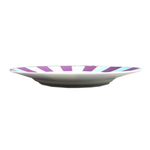 May include: A white ceramic plate with a purple and light blue striped design. The plate is slightly curved and has a rounded edge.