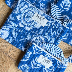 May include: Blue and white floral print quilted pouches and fabric. The pouches have a zipper closure and a small fabric tag that reads "Rooh London Handmade in India". The fabric has a similar floral pattern.