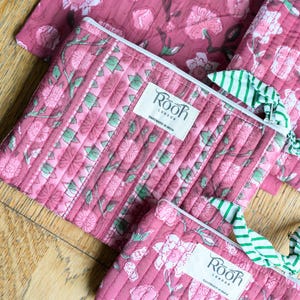 May include: Pink quilted pouches and fabric with a floral pattern. The pouches have white zippers and green and white striped pull tabs. The label on the pouch reads "ROOR LONDON HANDMADE IN INDIA."