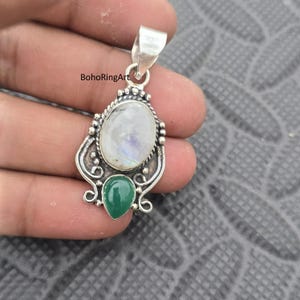 Puede incluir: Colgante de plata con una piedra lunar ovalada y una piedra verde en forma de lágrima. El colgante tiene un engaste de plata adornado con remolinos decorativos y detalles de cuentas. El texto "BohoRingArt" es visible.