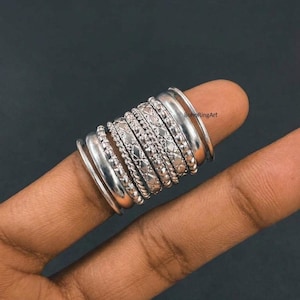 May include: A stack of nine silver-toned rings worn on a finger. The collection includes smooth bands, beaded bands, twisted rope-style bands, and bands with engraved diamond-shaped patterns. The text BohoRingArt is visible on the surface.