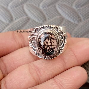 Könnte beinhalten: Silberring mit einem ovalen, klaren Edelstein mit schwarzen, linearen Einschlüssen. Der Ring hat eine verzierte Fassung mit einem Perlenrand und dekorativen Verzierungen. Der Text "BohoRingArt" ist sichtbar.