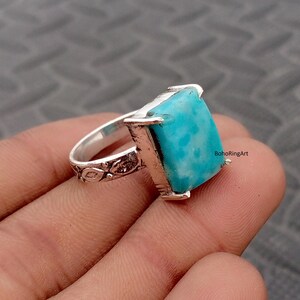 May include: A silver ring featuring a rectangular, bright turquoise stone set in a prong setting. The band has a textured, leaf-like pattern along the sides. The text BohoRingArt is visible on the side of the stone setting.