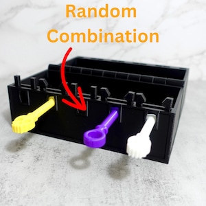 May include: A black box with a random combination lock. The lock has three slots, and each slot has a different colored key: yellow, purple, and white.