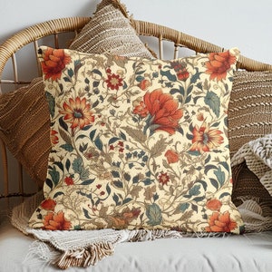 May include: A decorative throw pillow with a floral pattern in shades of orange, red, and green on a cream background. The pillow is sitting on a wicker couch with other pillows.