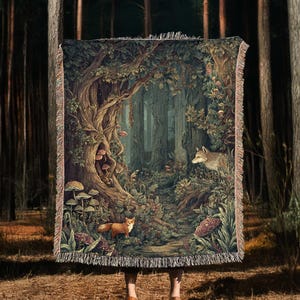 May include: A rectangular woven throw blanket featuring a detailed forest scene with a fox in the foreground, a wolf on the right, and large mushrooms growing near a gnarled tree trunk. The blanket has a fringed edge on the top and bottom sides.