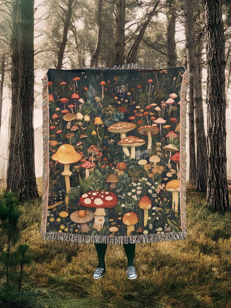 May include: A woven tapestry throw blanket featuring a dark green background with a colorful illustration of mushrooms and flowers. The blanket has a fringe border.