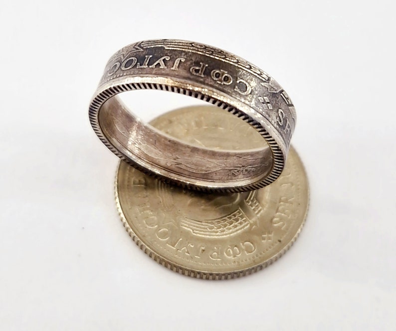 May include: A silver coin ring with the words "1 JPY" and "昭和 63 年" engraved around the band. The ring is sitting on top of a silver coin with the words "日本国" and "500 円" engraved on it.