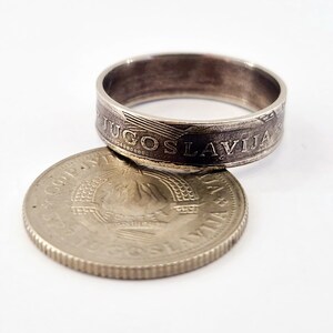 May include: A silver ring made from a Yugoslavian coin. The ring features the inscription "JUGOSLAVIJA" around the band. The coin is placed on top of a silver coin with a star and the inscription "JUGOSLAVIJA".