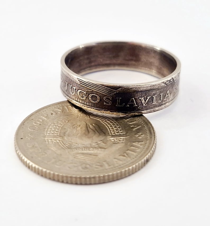 May include: A silver ring made from a Yugoslavian coin. The ring features the inscription "JUGOSLAVIJA" around the band. The coin is placed on top of a silver coin with a star and the inscription "JUGOSLAVIJA".