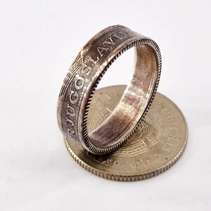 May include: A silver ring made from a vintage Yugoslav coin. The ring features the inscription "SRJUGOSLAVIJA" around the band. The coin is visible on the bottom of the image.