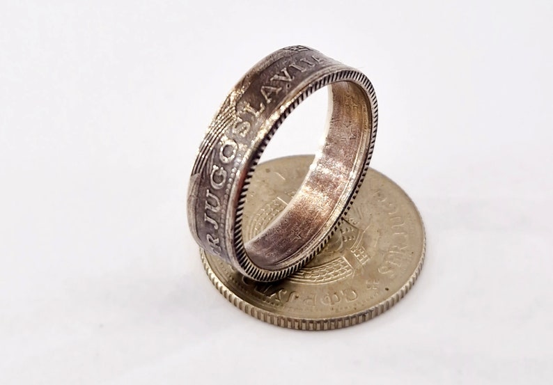 May include: A silver ring made from a vintage Yugoslav coin. The ring features the inscription "SRJUGOSLAVIJA" around the band. The coin is visible on the bottom of the image.