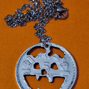 Peut inclure: Un collier en argent avec un pendentif en forme de pièce de monnaie en argent. La pièce a une valeur faciale de 5 et un motif de citrouille découpé.