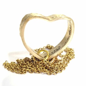 Peut inclure: Un collier avec un pendentif en forme de cœur en argent et une chaîne en or. Le pendentif est fait d'une pièce de monnaie pliée avec du texte visible sur l'extérieur.