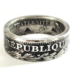Puede incluir: Un anillo de plata con la palabra "FRATERNITE" grabada en el interior. La banda exterior presenta la palabra "REPUBLIQUE" y un diseño de corona de laurel. El anillo tiene un aspecto vintage y desgastado.