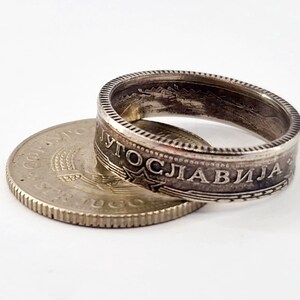 May include: A silver coin ring made from a Yugoslavian coin. The ring is made from the outer edge of the coin, and the inscription "JUGOSLAVIJA" is visible on the ring.