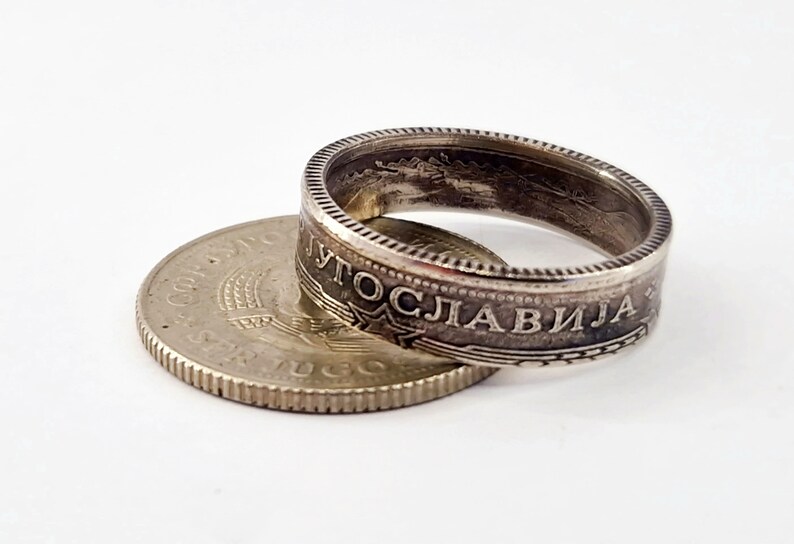 May include: A silver coin ring made from a Yugoslavian coin. The ring is made from the outer edge of the coin, and the inscription "JUGOSLAVIJA" is visible on the ring.