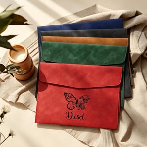 Puede incluir: Un conjunto de fundas para documentos en rojo, verde, beige, gris y azul marino. La funda roja presenta un diseño de mariposa y el nombre "Diesel". Las fundas tienen un aspecto texturizado similar al cuero.