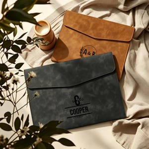 May include: Two rectangular document folders with envelope-style flaps. One folder is tan with a circular logo featuring the text A&R. The other folder is dark gray with a central logo featuring the letter C and the text COOPER.
