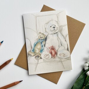 May include: A white teddy bear sits in a chair with two smaller teddy bears, one brown with a blue scarf and one red. The bears are drawn in pencil on a white card.