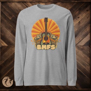 May include: A gray long-sleeve shirt featuring a guitar graphic with a sunburst background and the text "BMFS" in a retro font. The guitar is blue, yellow, and brown. The sunburst is orange and yellow.