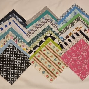 May include: A collection of 20 fabric squares with various patterns and colours, including black and white, green and white, blue and white, and pink and white. The squares are arranged in a pyramid shape.