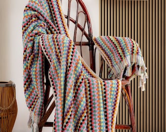 May include: A colorful striped towel with fringe hangs over a wicker chair. The towel is made of a soft, absorbent material and features a unique pattern of small circles.