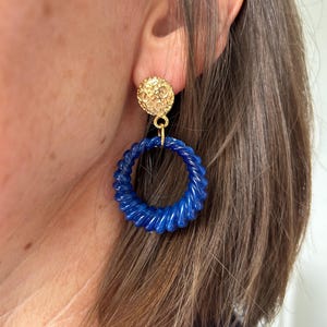 Peut inclure: Boucles d'oreilles statement dorées et bleues avec un cercle bleu torsadé et un dessus rond texturé doré.