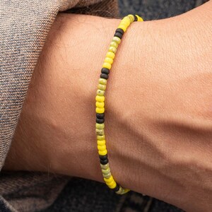 Op de afbeelding: Een armband met zwarte, gele en groene kralen.