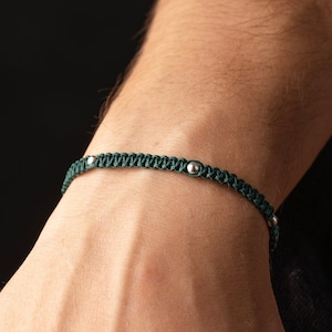 Op de afbeelding: Een donkergroene gevlochten armband met zilveren kralen.