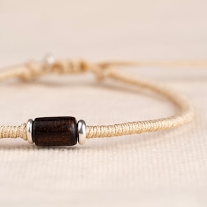 Op de afbeelding: Een eenvoudige armband gemaakt van beige koord met een donkerbruine houten kraal en zilveren accenten.