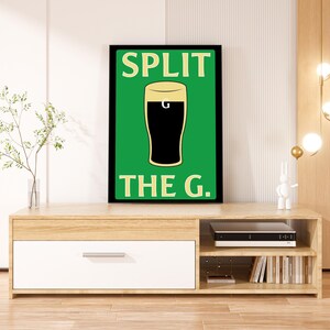 K&ouml;nnte beinhalten: Ein schwarzer gerahmter Druck mit gr&uuml;nem Hintergrund und wei&szlig;em Rahmen. Der Druck zeigt ein Glas dunkles Bier mit dem Text "SPLIT THE G." in Wei&szlig;.