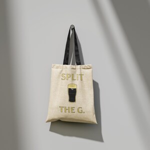 May include: A beige canvas tote bag with black handles. The bag has a graphic of a pint of beer and the text "SPLIT THE G."