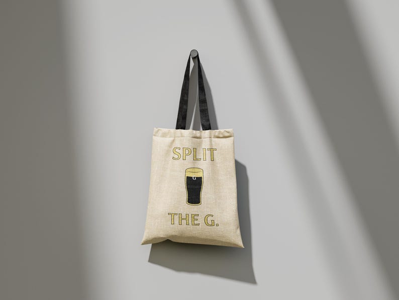May include: A beige canvas tote bag with black handles. The bag has a graphic of a pint of beer and the text "SPLIT THE G."