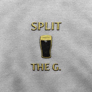May include: A gray t-shirt with the text "SPLIT THE G." in gold lettering. A black and gold illustration of a glass of beer is between the words.