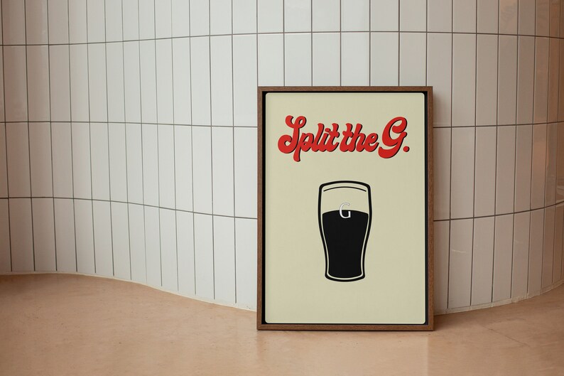 May include: A framed print with a cream background features a black and white illustration of a pint of beer. The text "Split the G." is in red, stylized lettering above the pint. The frame is a dark brown color.